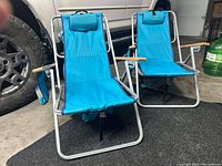 Two blue collapsible beach chairs with aluminum frames and wooden armrests placed on a garage floor.