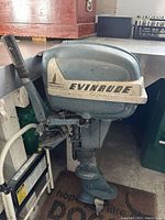 Side view of the Evinrude 7.5HP outboard motor with control handle and propeller visible. Motor painted blue-gray with white branding decal showing 'EVINRUDE' and 'AQUASONIC'. Shows signs of wear and dirt.