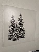 Photo showing an unframed canvas mounted on a wall displaying two snow-covered evergreen trees.