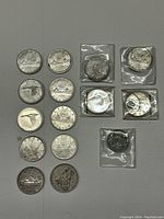 Wide view of 14 loose silver dollars and 5 sleeved coins laid out on table