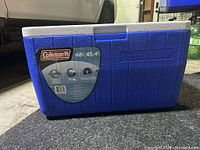 Blue Coleman cooler with capacity label attached, closed with white lid and textured sides.