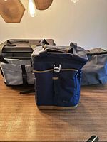 Photo showing three fabric collapsible cooler bags of varying sizes and colors on a wooden surface under warm lighting.