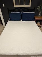Assembled bed with white quilted cover and navy pillows against dark wall