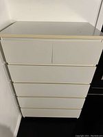 Photo showing front view of white IKEA dresser with six drawers in a corner against white walls.