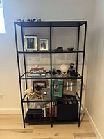 Front view of IKEA VITTSJ shelving unit showing black metal frame and glass shelves holding decorative items