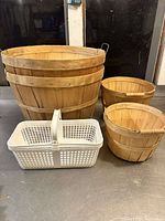 Photo showing a lot of four baskets: one large wooden apple bushel basket, two smaller wooden berry picking baskets, and one white plastic basket with handle.