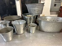 Photo of nine tin planters and buckets of various sizes and shapes, including a large oval planter marked 20L and several smaller buckets with galvanized finishes.