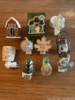 Lot of 11 Bath and Body Works and Scentsy plug-in holders and warmers on brown wooden surface.