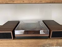 Record player with dust cover closed, showing wooden case and two wooden speakers on sides.