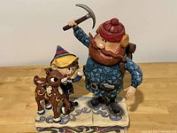 Photo showing full clear view of the painted statue featuring Cornelius holding an ice pick, Hermie, and Rudolph standing closely together on a decorated base.