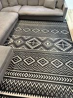 Full view of the rug placed under sectional sofa, showing the large black and white geometric pattern.