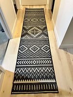 Full length photo of the black and white geometric Arizona pattern runner rug laid on light hardwood floor in a hallway.
