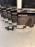Five boxed sets of NOMA Starry Lights with a power adapter on a grey surface.