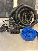 Full view of Mastercraft submersible pump with connected black corrugated hose and separate coiled blue flat hose.