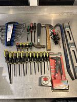 Overhead shot showing all tools laid out on a metallic surface including wrenches in a holder, screwdrivers, two hammers, pry bars, a tape measure and a rivet tool in packaging.