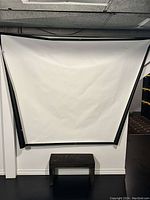 Photo shows white projection screen mounted on wall with visible metal grommets in corners and rolled storage marks.