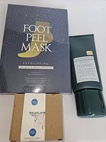 Photo of black box labeled 'Foot Peel Mask' containing 2 pairs of foot masks, natural soap box, and green tube of hair mask.