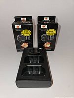 Two boxed replacement Li-ion batteries LP-E6N standing behind a black dual bay stand charger with two slots and indicators on top.