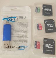 Photo showing a blue USB 3.0 external hard drive flash drive sealed in plastic packaging and three 1TB Micro SD cards with their corresponding SD card adapters on a plastic holder.