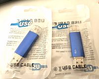 Two blue 1TB USB flash drives in original clear plastic packaging labeled 'USB Cable' showing front view of drives with dual connectors caps.