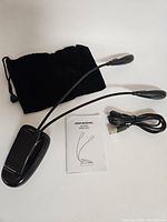 Photo showing two black clip-on LED lamps with flexible gooseneck arms, USB charging cable, user manual, and a black storage pouch.