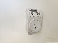 Photo of the plug-in floor heating thermostat plugged into a wall outlet showing digital display and control buttons.