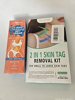 Box of 2-in-1 Skin Tag Removal Kit and Body Slimming Hot Cream showing product branding and usage information.