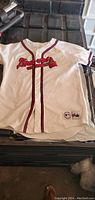 Front side of Atlanta Braves white baseball jersey with red and navy piping and Braves script logo.
