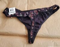 Black bikini underwear with floral print and lace trim, front view with tag visible.