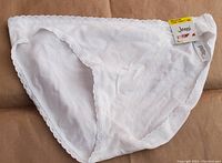 Front view of bright white cotton women's underwear with lace trim and attached tags, size medium.