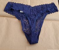 Front view of navy sea blue lace thong underwear laid flat, showing floral lace design and waistband.