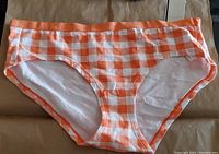 Front view of the orange and white gingham checkered bikini style underwear, showing the elastic waistband and fabric pattern.