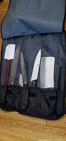 Photo showing 5 utensils including 3 heavy-duty cutters with metal blades, 1 white plastic baking spatula with maroon handle, and the roll-up black storage holder