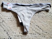White ribbed fabric thong with black and white branded waistband flat on carpet showing tags