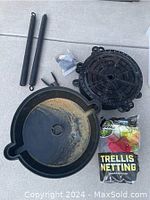 Photo shows all items in the lot including two round black watering trays, sealed pack of trellis netting, tubing stakes, wire cutters, and cable ties arranged on a floor.