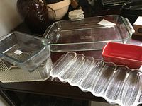 Multiple glass and ceramic baking dishes including large Pyrex rectangular dish, fire king ribbed casserole, refrigerator dish without lid, small red bread baker, and red cornbread dish.