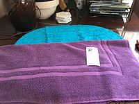 Purple rectangular bath mat lying on turquoise oval bath mat on wooden floor