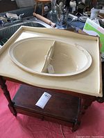 Top view of vintage child's wash stand showing cream ceramic divided basin inset into wooden stand. Towel racks on sides and pull-out drawer below visible.