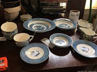 Full view of partial Currier & Ives china set including bowls, cups, saucers, and creamers on a dark surface.