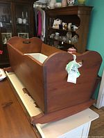 Doll cradle showing side and interior with cushion, solid wood construction and carved handles