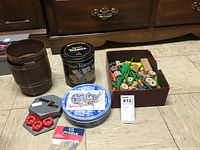 Overall view of all games included in the lot arranged on floor: Tinker Toys parts in box, Barrel of Monkeys barrel, Drive You Nuts game parts, IQ Puzzle box, and Sport Teasers tin.