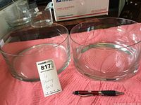 Two clear glass bowls on pink fabric with a pen for scale, showing size and condition.