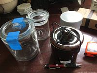 Four small containers with lids, including glass and metal components, shown on a dark wood surface.