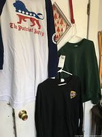 Photo showing three long sleeve shirts hanging: white/navy 'The Patriot Party' XL shirt, green sweatshirt size L, and black Maryland Medevac Team XL shirt.