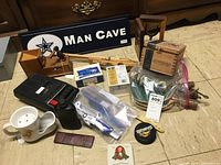 Wide angle showing the collection of man cave and vintage items including wooden toys, decor, and collectibles spread out on floor.
