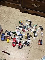 Photo shows approximately 33 small toy cars of varied racing types and colors spread on a tiled floor.