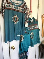 Photo showing the short sleeve top, long sleeve zip top, and elastic waist pants with southwestern patterns hanging on a white door.