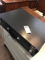 Full closed rectangular black metal photographer's case with handle placed on a piece of furniture.