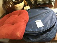 Navy blue pop up laundry/storage bag and wine-colored padded chair cushion placed side by side on a wooden table.