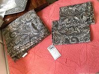 Top sheet and two pillowcases spread on quilt showing paisley pattern and small repair on top sheet